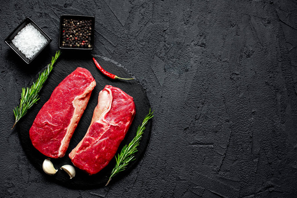 Бифштекс из сырой говядины со специями и травами на черном фоне - Фото, изображение