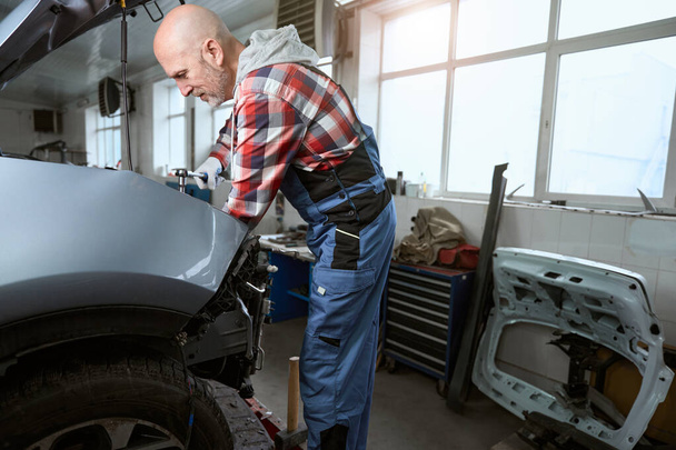 Auto repairman at the workplace repairs a car, a man uses a special tool - Fotó, kép