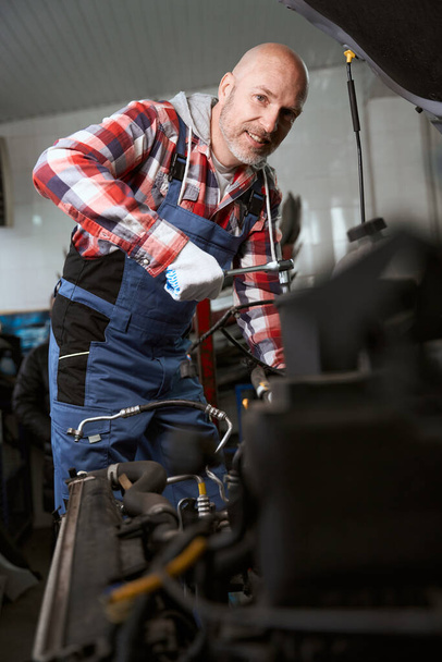 Handsome man in a plaid shirt is repairing a car, the master uses a special tool - Photo, Image