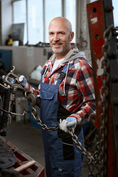 Man in a plaid shirt stands in a car repair shop with a carbine and a chain - Foto, afbeelding