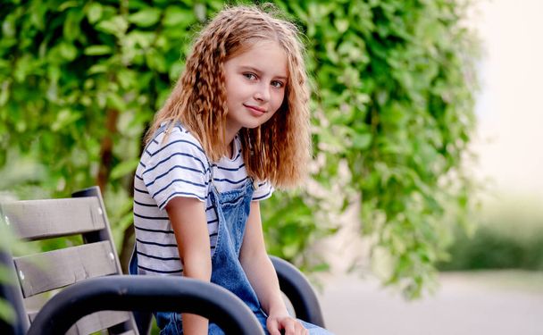 Beautiful preteen girl in city in summertime closeup portrait. Pretty female kid looking at camera in sunny day with blurred background - Zdjęcie, obraz