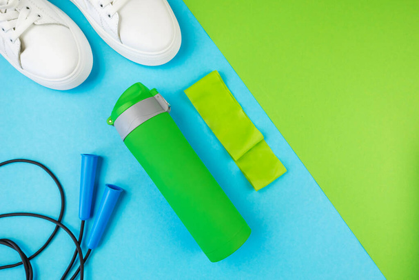 Sports concept. Top view photo of white sneakers with sports bottle jump rope and elastic band on blue green background - Foto, Bild