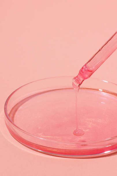 Pipeta com líquido rosa pingando. Ou ouro rosa. Em cima de uma placa de Petri com líquido rosa. Sobre um fundo rosa. Laboratório, química, medicina. Investigação cosmética. purpurina. - Foto, Imagem