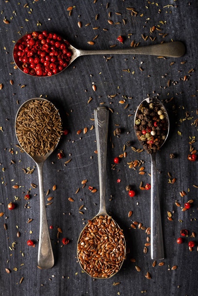 Old spoons with various seeds and spices on black background. Flat lay. Top view. Food concept. Dark mood food photography. - Фото, изображение