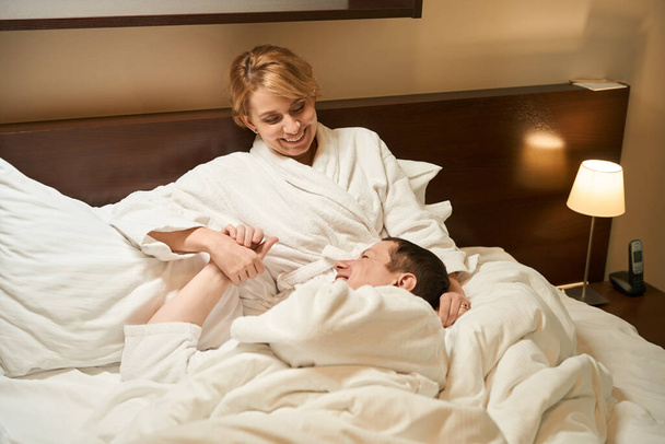 Middle aged couple enjoy relaxing on big bed, people in bathrobes - Foto, afbeelding