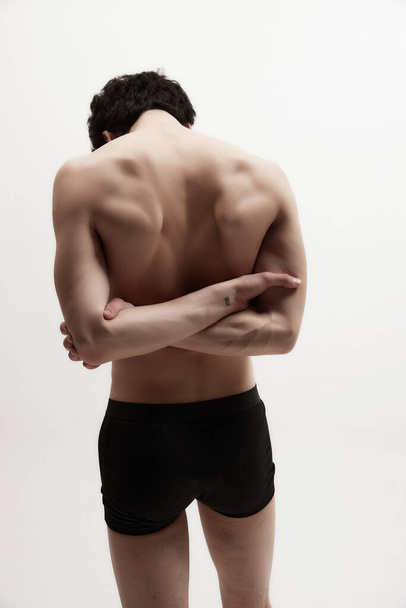 Relief, strong, muscular back. Rear view of young man posing shirtless, in black underwear against white studio background. Healthy spine. Concept of male body aesthetics, style, fashion, mens beauty - Photo, image