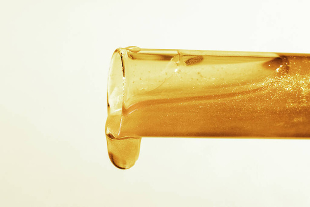 Reagenzglas mit fließendem Gold. Glitzer, Lack, Flüssigkeit. Pailletten. Laboruntersuchungen von Kosmetika und Flüssigkeiten. Aktuelles Gel mit Gold - Foto, Bild