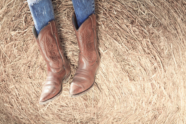 Western style image of cowgirls legs in jeans and boots on dese - Foto, afbeelding