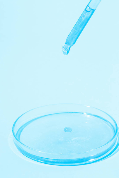 Pipeta con líquido azul goteante. En una placa de Petri con líquido azul. Sobre un fondo azul. Laboratorio, química, medicina. Investigación cosmética. brillar. - Foto, imagen