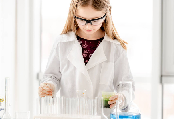 Chica haciendo experimento de química científica usando gafas de protección. Colegiala con equipo y líquidos químicos en la lección escolar - Foto, Imagen