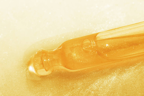 Una pipeta cosmética se encuentra en un líquido dorado. O un líquido amarillo con purpurina. Investigación de laboratorio de cosméticos, gel, medicina. Química - Foto, imagen