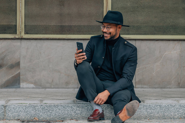 Λατίνος άνδρας με κινητό τηλέφωνο κάθεται στο δρόμο - Φωτογραφία, εικόνα