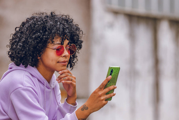 афро девушка с солнцезащитными очками и мобильным телефоном - Фото, изображение