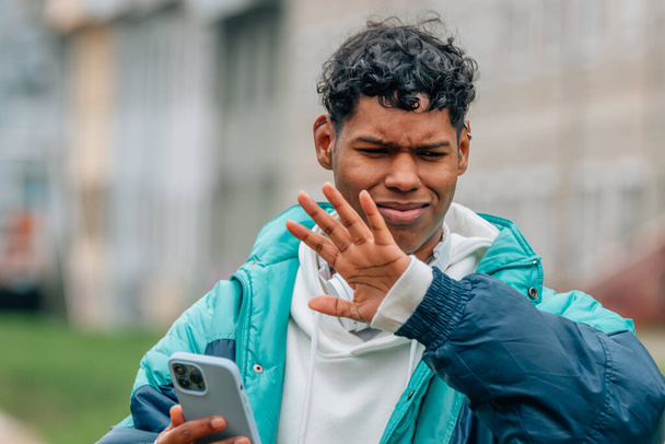 Młody człowiek z telefonem komórkowym na ulicy z wyrazem odrzucenia - Zdjęcie, obraz