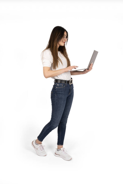 Using laptop, full length body size side view of woman using laptop. Teen, attractive girl holding notebook in hands browsing internet. Standing over isolated white background, copy space.  - 写真・画像