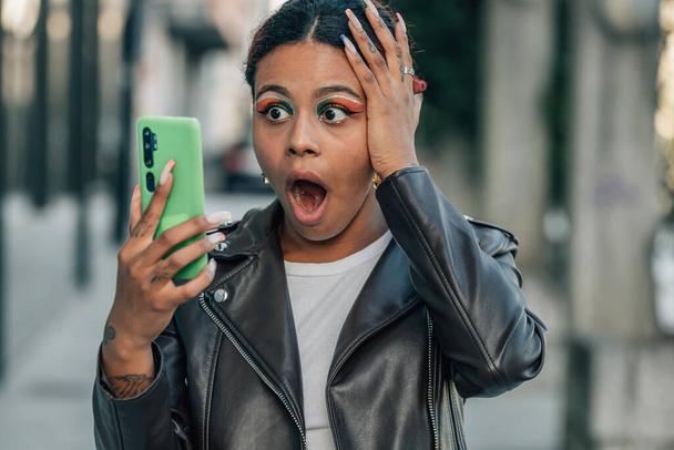afro americana chica en la calle con teléfono móvil y expresión sorprendida - Foto, imagen