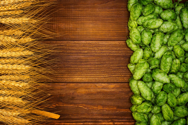Beer brewing ingredients, green hop cones, and golden wheat ears on a wooden table with space for your object or text - Photo, Image