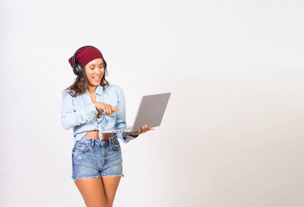 Beautiful latin woman listening to music and dancing joyfully with headphones on the laptop - 写真・画像