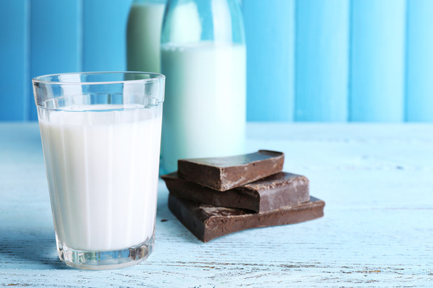 Glass and bottles of milk with chocolate chunks on color wooden planks background - Foto, imagen