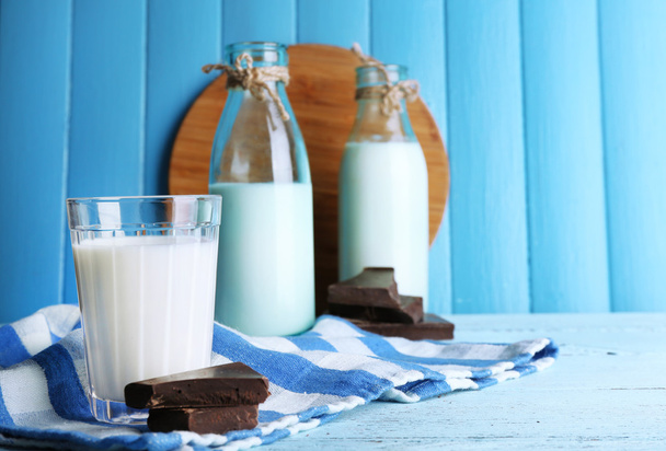 Glass and bottles of milk with chocolate chunks on stripped napkin and color wooden planks background - Foto, Imagem