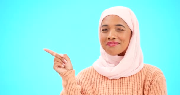 Mujer, señalando con el dedo y el espacio para el feliz anuncio musulmán con la mano para maqueta. Mujer islámica con hijab y cara con sonrisa para la venta, promoción o colocación de productos en el estudio de fondo azul. - Imágenes, Vídeo