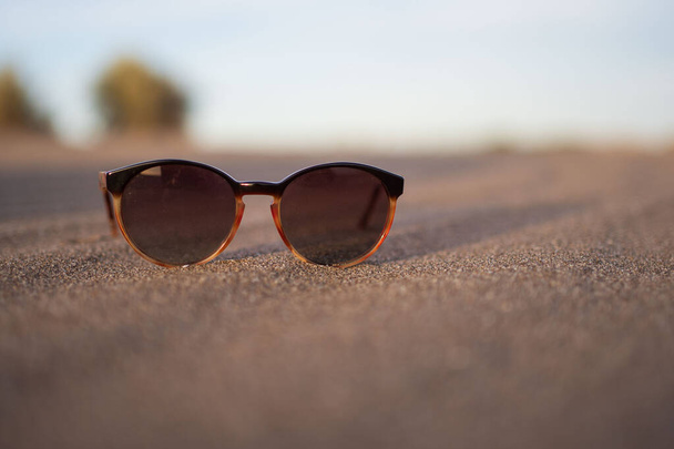 Napszemüveg nyugszik a homokban egy dűne naplemente fény - Fotó, kép