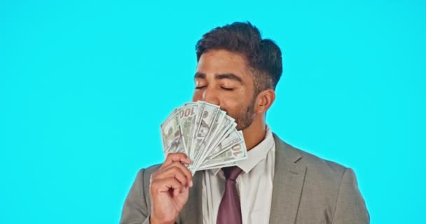 Üzletember, dollár rajongó és stúdió elszigetelve egy kék háttérképpel. Készpénz, nyertes és arc portré boldog indiai személy illata vagy szippantás pénz után lottó, bónusz díj vagy pénzügyi szabadság - Felvétel, videó