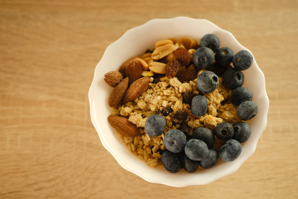 close-up top view on healthy food white cup on light table, oatmeal, blueberries, nuts, almonds, peanuts , raisins, dried fruits, raw food diet, vegetarian food - Foto, afbeelding