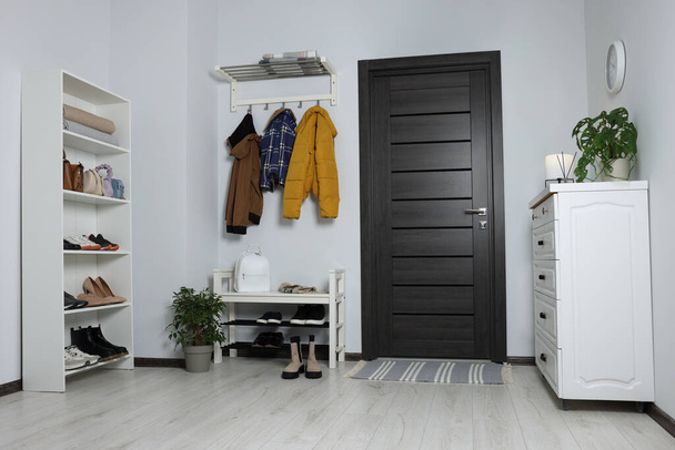 Beautiful hallway interior with coat rack, chest of drawers and shoe storage bench near wooden door - Foto, Imagen