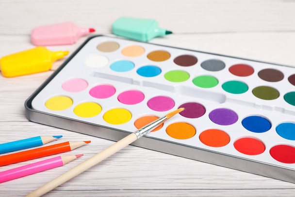 Watercolor palette with brush, colorful pencils and markers on white wooden table, closeup - Foto, immagini