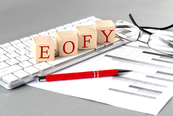 キーボード上の木製のキューブにグレーの背景にチャートで書かれたEOFY - 写真・画像