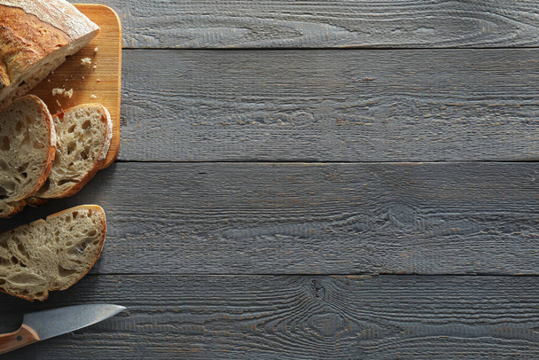 Food photography. Cut freshly baked bread and knife on wooden table, flat lay with space for text - Zdjęcie, obraz