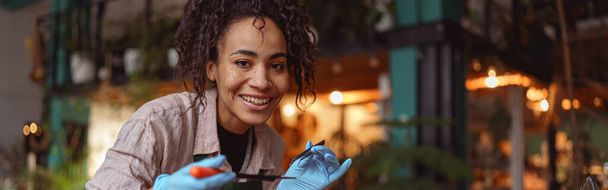 Χαμογελαστή γυναίκα ανθοπώλης που κάνει χυμώδη σύνθεση φυτών στο στούντιο ανθοκομικού σχεδιασμού. Υψηλής ποιότητας φωτογραφία - Φωτογραφία, εικόνα