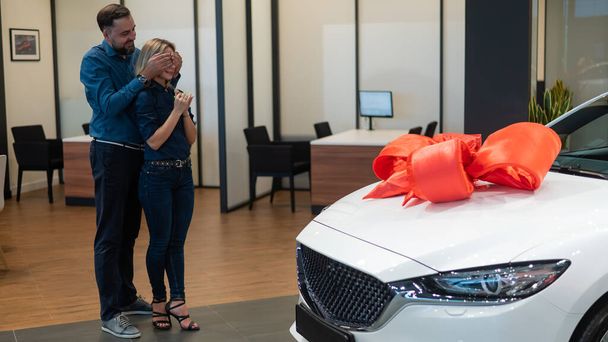 A bearded man makes a gift to his beloved wife in the form of a new white car - Fotó, kép