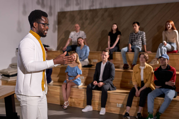 Side View Of Nice African American Teacher In White Clothing Lecturing Presenting Speech Gesturing With Hands, Discussing Important Theme With Students, Group Of People In The Background - Fotó, kép