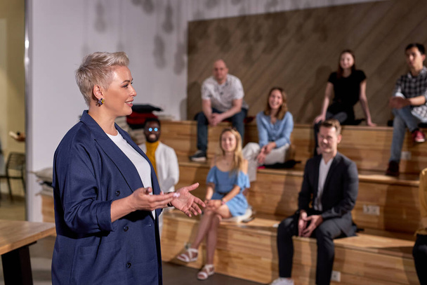 Pleasant Female speaker giving talk in conference hall at business meeting event. Group of people in audience at conference hall, listening to lesson. Business and entrepreneurship. copy space - Foto, Bild