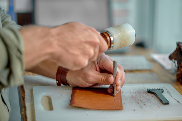 young mans hands punching holes in the leather with a punch.Tools for leather craft.side view - Fotografie, Obrázek