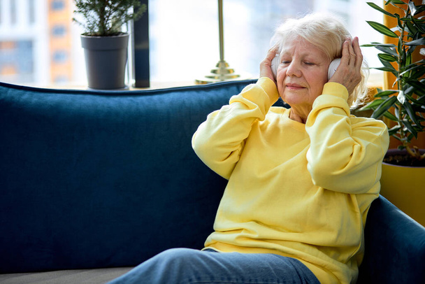 Old people, emotion and technology concept: elderly caucasian woman listen to music with headset, enjoy having rest alone, at weekends. pretty lady with grey hair in casual clothes - Fotografie, Obrázek