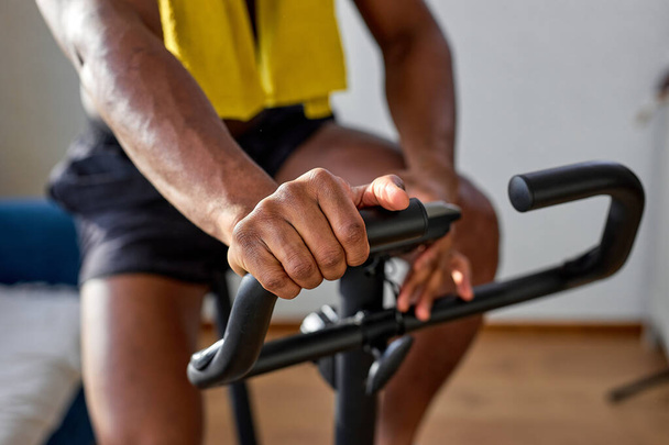 Indoor cycling, spinning cycling training. Sports training on a stationary exercise bike. cropped muscular african guy engaged in cardio workout training, shirtless male body. focus on hands - 写真・画像
