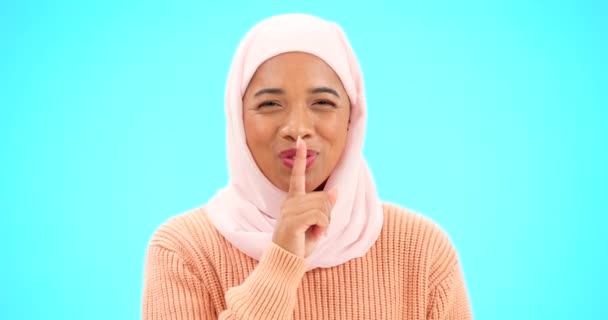 Moslim vrouw, vinger op de lippen en geheim met de hand op de mond voor mockup, reclame of promotie. Islamitische vrouw met hijab, gezicht emoji of lach te koop, roddel of verrassing op studio blauwe achtergrond. - Video