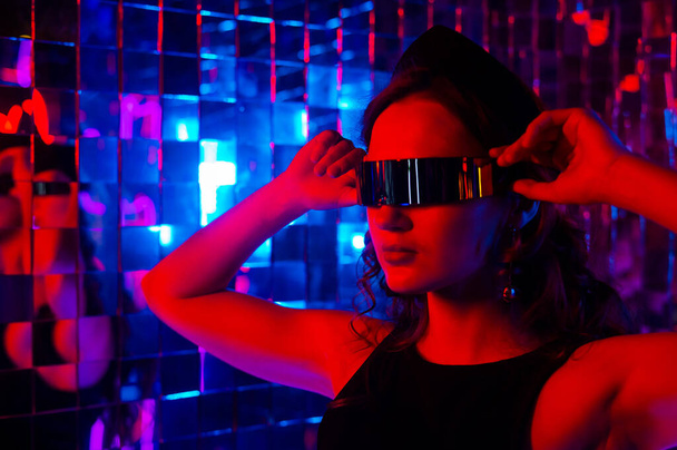 Close-up portrait of a caucasian woman in sunglasses in neon light against a mirror wall - Foto, Imagem