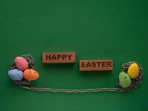 Paaseieren op groene ondergrond met metalen ketting. Pasen kaart ontwerp met Happy Easter tekst en kopieer ruimte. Een nest voor een ei gemaakt van metalen ketting. Pasen gereedschap, werknemer concept. - Foto, afbeelding
