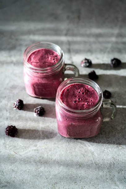 Two mugs with blackberry smoothies on a gray background. Delicious dessert for a healthy diet. - Foto, Bild