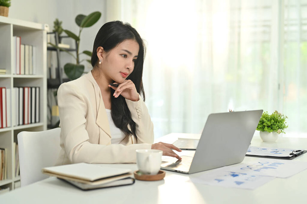 魅力的なアジアの女性起業家は、ラップトップコンピュータを介してインターネット上で通信し、オンラインクライアントとチャット. - 写真・画像