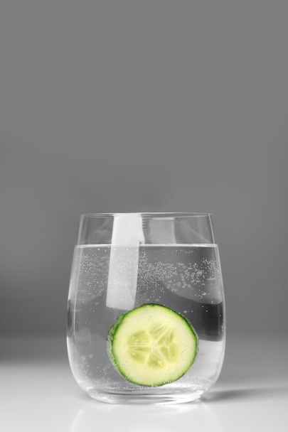 Glass with fresh cucumber on grey background - Foto, afbeelding