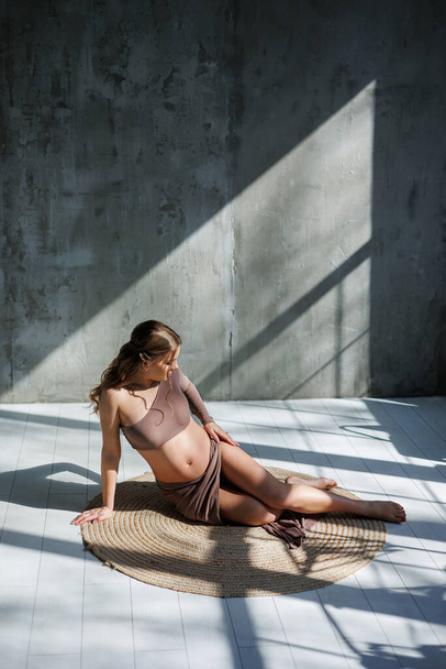 Улыбающаяся молодая беременная женщина в верхней и юбке позирует в студии и гладит живот. Беременная женщина. Счастливая беременность - Фото, изображение