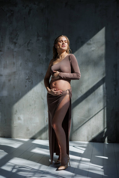 Νεαρή έγκυος με μπεζ μπλούζα και φούστα. Μητρότητα, εγκυμοσύνη, χώρος αντιγραφής. Μόδα για την εγκυμοσύνη. Ευτυχισμένη περίοδος της εγκυμοσύνης - Φωτογραφία, εικόνα