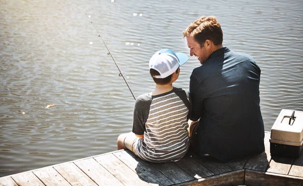 Geniet je van de visreis tot nu toe. Achteraanzicht van een vader en zijn zoontje die samen vissen - Foto, afbeelding