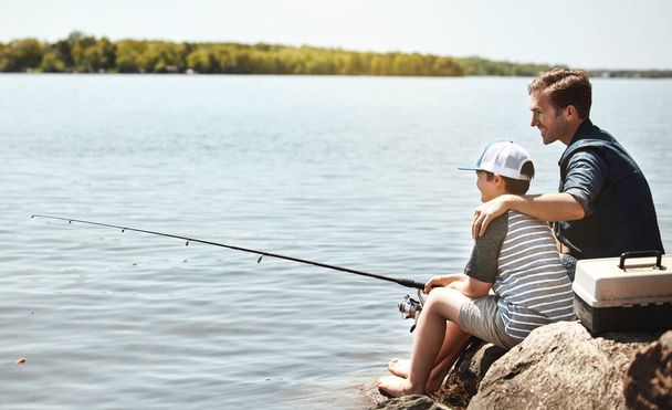 Birlikte ilk balık avlama maceralarının tadını çıkarıyorlar. Bir baba ve küçük oğlu birlikte balık tutuyorlar. - Fotoğraf, Görsel