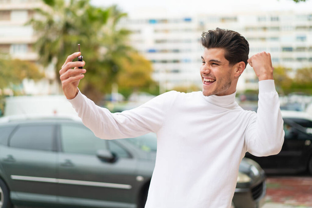 Young caucasian man holding car keys at outdoors celebrating a victory - Foto, Imagen